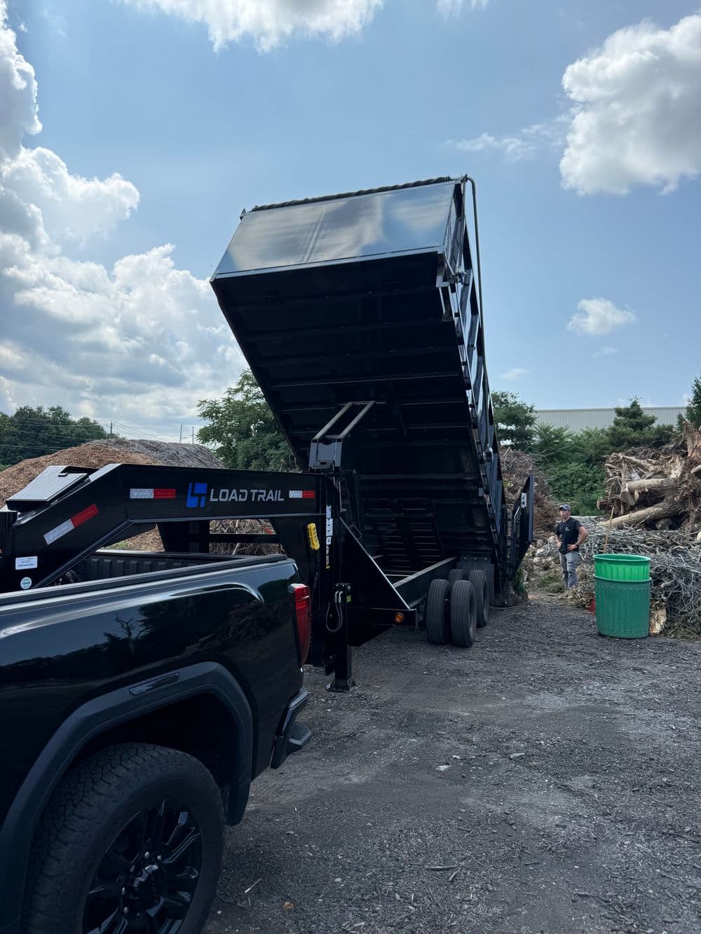 Black Load Trail dump trailer unloading materials under a bright sky at a construction site.